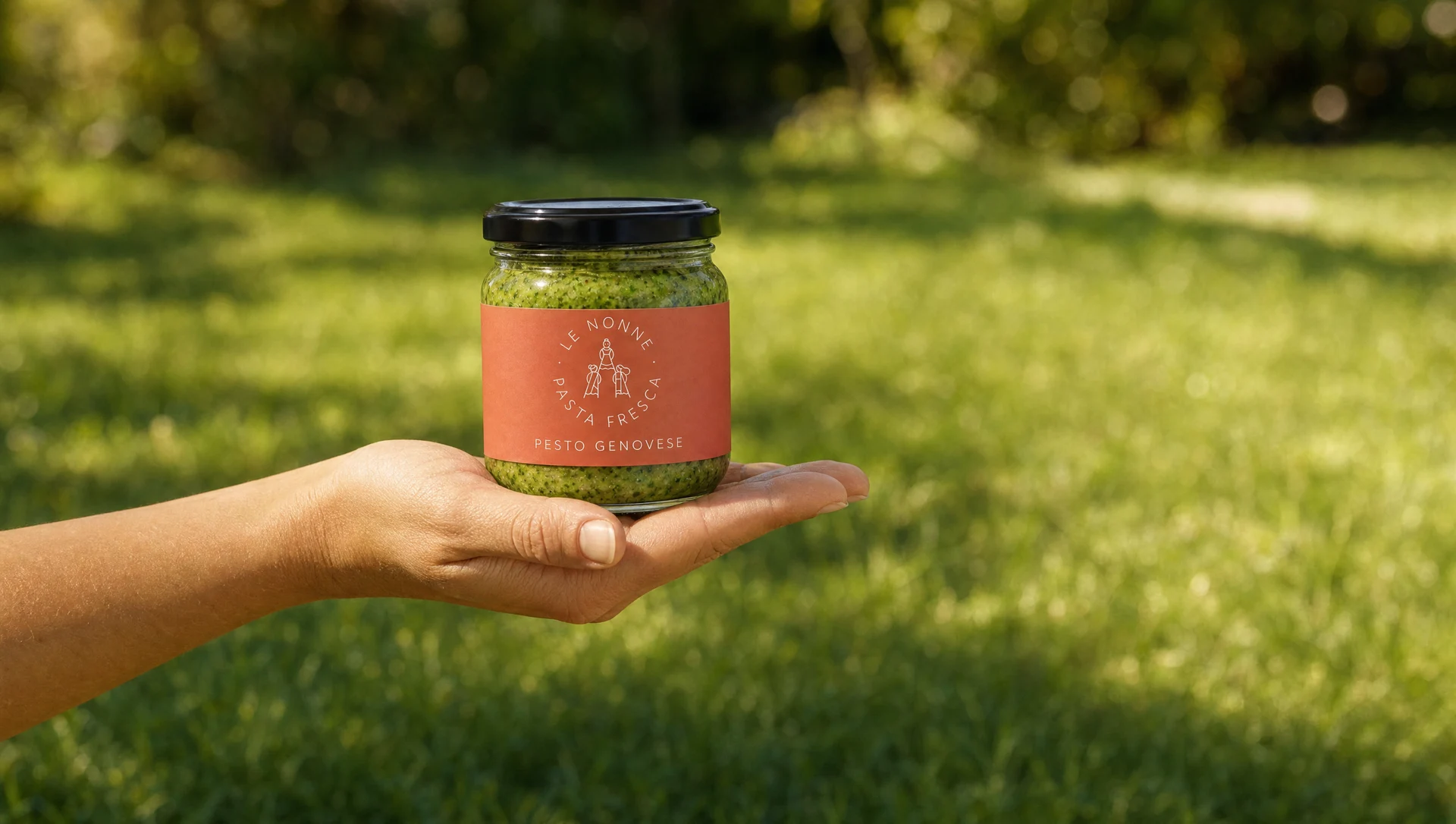 Ruka drži teglu Le Nonne Pesto Genovese sosa ispred zamućene zelene pozadine